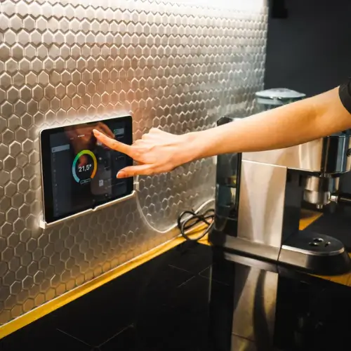 Hand operating a smart home touchscreen panel on a modern kitchen wall – Rajvar Technologies